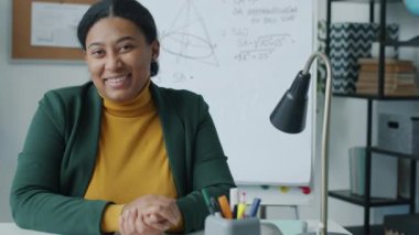 Sınıfta oturmuş kameraya gülümseyen Afrikalı Amerikalı kadın matematik öğretmeninin yavaş çekim portresi. Halk ve mesleki meslek kavramı.