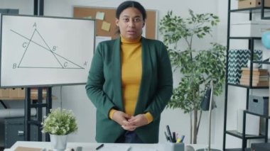 İçeride çalışan, konuşan ve kameraya bakan matematik öğretmeninin portresi. Arka planda teknik çerçeve olan elektronik tahta.