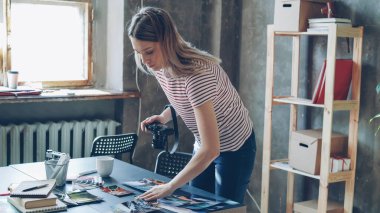 Tablo üzerinde görüntülenen seyahat renkli resimlerden ateş etmek Digital fotoğraf makinesi kullanarak genç çekici kadın blogger. O fotoğrafları taşıma ve farklı kolaj yapma. Loft stil office arka planda.