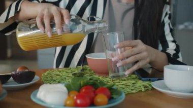 Kadın eli bardağa meyve suyu dökerken ve evde kahvaltıda içerken yakın plan. Yaşam tarzı ve sağlıklı beslenme konsepti.