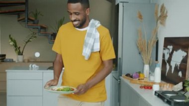 Afro-Amerikalı mutlu bir adam mutfakta kahvaltı yapıyor ve sabahları akıllı telefon kullanıyor. Gençlik yaşam tarzı ve beslenme konsepti.