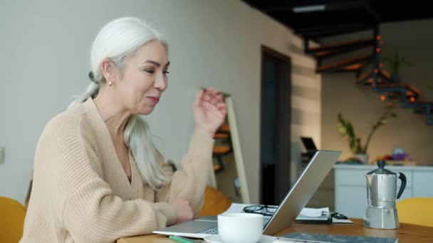 成熟的女士在家里用笔记本电脑在线视频通话 一边在厨房里一边说话一边挥手 交流和社会疏离概念 — 图库视频影像