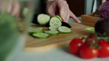 Ev hanımı taze çiğ sebzelerden salata pişirirken, kadın ellerinin mutfakta bıçakla salatalık dilimlediği yakın plan. Sağlıklı yemek ve aşçılık konsepti.