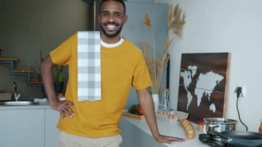 Mutfakta kameraya bakarak gülümseyen neşeli genç adamın yavaş çekim portresi. Ev hayatı ve olumlu duygu kavramı.