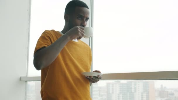 非洲裔美国人喝咖啡 从全景窗口看城市 独自站在公寓里 人与生活方式概念 — 图库视频影像