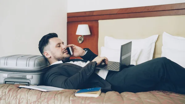 Fiatal Szakállas Üzletember Feküdt Ágyban Bőrönd Beszélő Telefon Laptop Szállodai — Stock Fotó