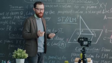 Profesör konferans veriyor ve kamerayla video kaydediyor. Çevrimiçi vlog için içerik oluşturuyor. Genç adam konuşuyor ve tahtaya işaret ediyor..