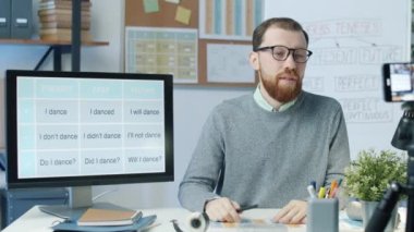 Sınıfta akıllı telefon kamerasıyla video dersi kaydediyor. İngilizce konuşan ve el kol hareketi yapan genç adam..