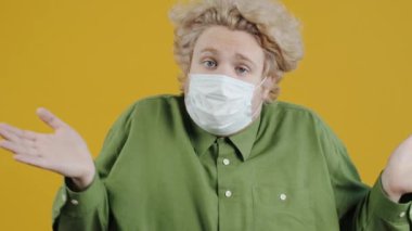 Tıbbi yüz maskesi takan yorgun ve mutsuz bir gencin portresi. Sarı arka planda kendini güvensiz hissediyor. İnsanlar ve salgın konsepti.