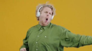 Yaratıcı genç adam portresi şarkı söylüyor ve dans ediyor sarı arka planda kulaklıkla müzik dinliyor. Halk ve kültür kavramı.