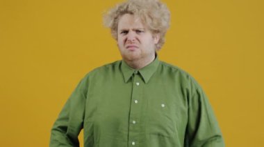 Kırgın bir gencin portresi kollarını kavuşturup, sarı arka planda kameraya bakarken dilini gösteriyor. Olumsuz duygular ve ifadeler kavramı.