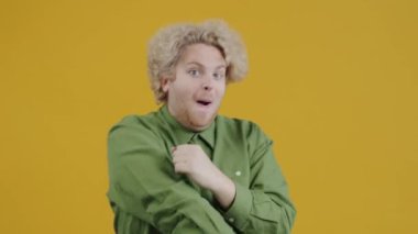 Dans eden ve sarı arka planda kameraya bakan komik genç adamın yavaş çekim portresi. İnsanlar ve duygular.