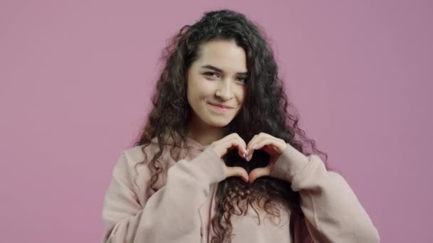 手でハートジェスチャーをしてピンクの背景にエアキスを送る魅力的な女の子の肖像画 ロマンチックな若者と感情の概念 — ストック動画