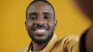 Sarı arkaplanda kameraya bakarken konuşan yakışıklı Afro-Amerikalının yakın plan portresi. İnsanlar ve iletişim konsepti.