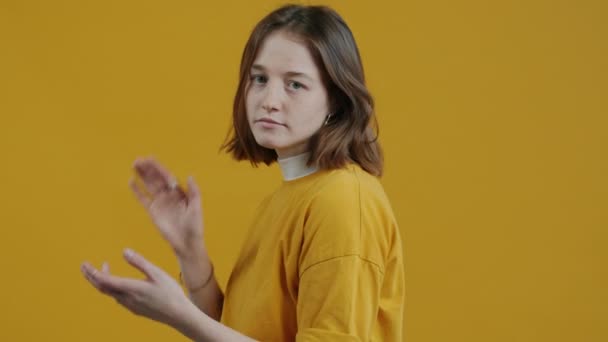 恼怒的年轻女子出于义务拍拍双手 看着站在黄色背景上的相机的慢动作肖像 人与表达的概念 — 图库视频影像