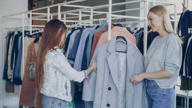 Tezgâhtar genç kadın yardım, onun güzel ceket getirmek ve modeli hakkında söylüyorum. Müşteri, pazarlamacı ile sohbet ederken diğer giysi Rails ile karşılaştırarak dokunuyor
