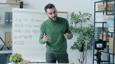 Gemiye kimya formülü yazan fen öğretmeni tripoddaki modern kamerayı kullanarak sınıftaki internet vlog 'unun içeriğini kaydediyor.