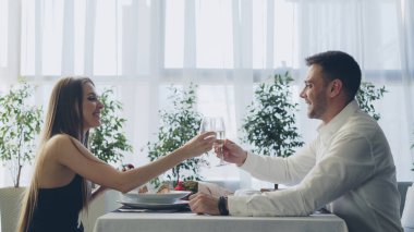 Genç ve yakışıklı bir adam şık bir restoranda yemek yerken kız arkadaşıyla kadeh tokuşturup şampanya içiyor..