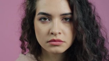 Genç bir kadının yakın plan portresi kendini çekerken ve pembe arka planda kameraya bakarken görülüyor. İnsanlar ve ifadeler kavramı.