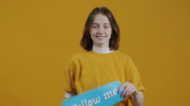 Milenyum yaratıcı portresinin yavaş çekimde çekilmiş hali Follow Me tabelası ve sarı baackground 'da davetiye çıkartma hareketi. Sosyal medya ve günlük tutma kavramı.