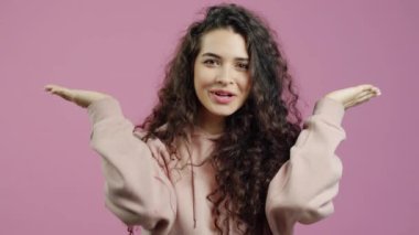 Elleriyle yüzünü saklayan neşeli kadının yavaş çekimde portresi. Sonra da pembe arka planda saklambaç oynarken gülümseyen kameraya bakıyor.