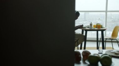 Afro-Amerikan halkının portresi yemek yerken ve kulaklıklarda müzik dinlerken panoramik pencere arka planında