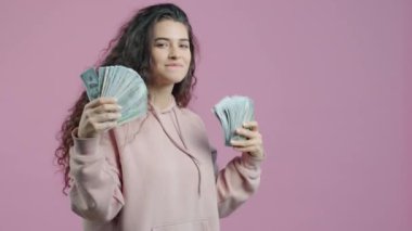 Mutlu genç kadın elinde parayla dans ediyor zenginliğin tadını çıkarıyor pembe arka planda eğleniyor. Para ve olumlu duygular kavramı.