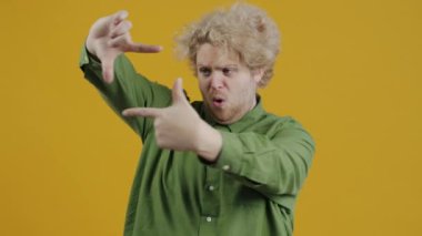 Yaratıcı genç adamın portresi odaklanmış el hareketi yapıyor ve sarı arkaplandaki kameraya bakıyor. İnsanlar ve ifadeler kavramı.