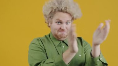 Alkışlayan ve sarı arka planda duran kameraya bakan mutlu genç adamın portresi. Başarı ve onay kavramı.