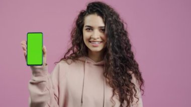 Güzel bir kızın portresi, elinde yeşil krom anahtar, akıllı telefon, alete bakıyor ve pembe renk arka planına karşı gülümsüyor..