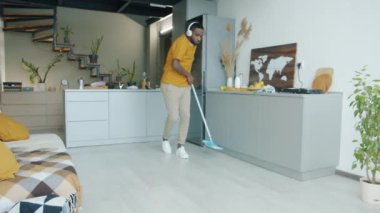 Kulaklık takan, mutfakta yerleri paspaslayan, plastik paspasla dans eden ev işi yaparken eğlenen adam. Yaşam tarzı ve ev kavramı.