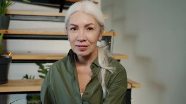 Evde merdivenlerde oturmuş gülümseyen neşeli yüzüyle kameraya bakan güzel olgun bir kadının yavaş çekimde portresi. İnsan duyguları ve apartman konsepti.