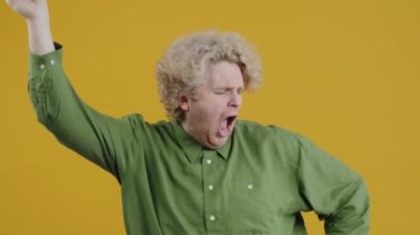 Heyecanlı adamın yavaş çekim portresi. Tek başına dans eden, sevinçten çığlık atan ve sarı arka plandaki kameraya bakan adam. Faaliyetler ve yaşam tarzı konsepti.