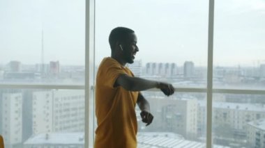 Büyük pencereli, akıllı telefonlu, kablosuz kulaklıklı neşeli adamın dairede dans etmesi. Halk ve gençlik kültürü kavramı.