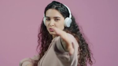 Pembe arka planda dans eden ve yalnız eğlenen, kulaklık takan çekici genç bayanın yavaş çekimde portresi. İnsanlar ve eğlence konsepti.