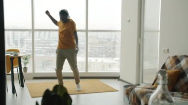 Neşeli dansçıların mutfakta kulaklık takıp büyük pencere arkasında dans etmesinin yavaş çekimi. İnsanlar ve eğlence konsepti.