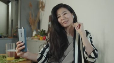 Neşeli Asyalı kadın konuşuyor, el sallıyor ve yemek sırasında internette video görüşmesi yapıyor. Yemek yiyip sohbet eden bir kadın..