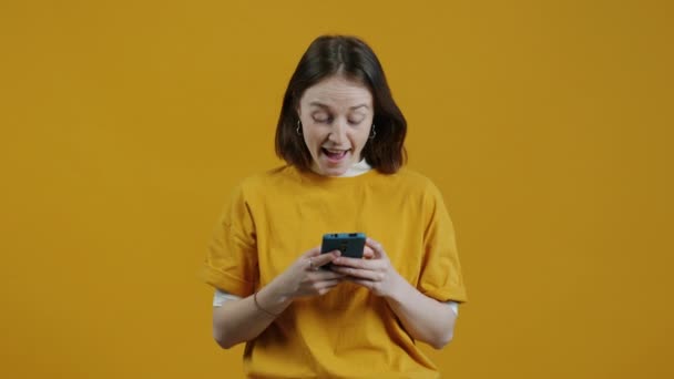 一个快乐的年轻女人的画像 收到指向智能手机的信息 然后在黄色背景下发短信和微笑 人与通信概念 — 图库视频影像