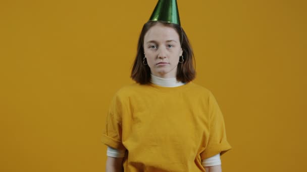 不幸な若い女性の肖像画パーティーホーン吹いて黄色の背景に明るい帽子を脱いで 負の感情と悪い休日の概念 — ストック動画