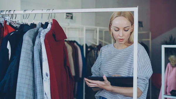 若い実業家はレールの上の衣服をチェック 彼女の衣料品店でタブレットを使用しています 彼女は価格とラベルのチェックは 画面に触れると入力します 成功したスタートアップのコンセプト — ストック写真