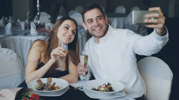 매력적 연인들은 식당에서 로맨틱 식사를 하면서 스마트폰을 사용하여 샴페인 잔으로 — 스톡 사진