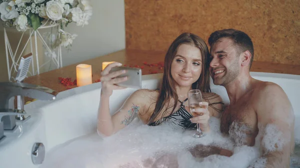 Sevimli Genç Çift Selfie Küvette Yıkanırken Smartphone Kullanarak Köpüklü Şampanya — Stok fotoğraf