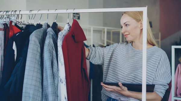 若い実業家はレールの上の衣服をチェック 彼女の衣料品店でタブレットを使用しています 彼女は価格とラベルのチェックは 画面に触れると入力します 成功したスタートアップのコンセプト — ストック写真