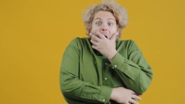 Şaşırmış bir adamın portresi, kameraya bakıp ağzını kapatıyor sonra baş parmak işareti yapıyor ve sarı arkaplana gülümsüyor. İnsanlar ve duygular.