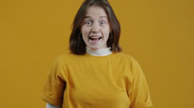 Heyecanlı genç bir kadının yavaş çekim portresi mutluluğu ifade ediyor sarı arka planda şaşkınlık ve sevinç dolu. İnsanlar ve duygular.
