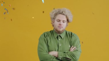 Kollarını kavuşturmuş üzgün genç bir adamın portresi. Sonra yukarıdan renkli konfetilerin düşüşünü ve sarı arka planda gülümsemesini izlemek.