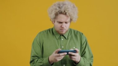 Akıllı telefonunla video oyunu oynayan duygusal adamın portresi sarı arkaplana karşı öfkesini gösteriyor. İletişim ve olumsuz duygular kavramı.