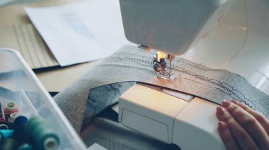 Modern elektrikli dikiş makinesi çalışma Tekstil parça dikiş close-up. Kızlar manikürlü elini, kağıt ve renkli dikiş ipliği skeçler görülebilir.