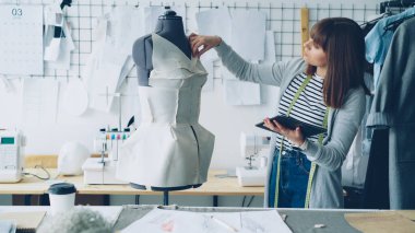 Girişimci tasarlama genç kadın moda giyim mankeni terzilik için pinned denetlerken tablet ile çalışıyor. Modern teknolojileri kavramı üretim kıyafetler.
