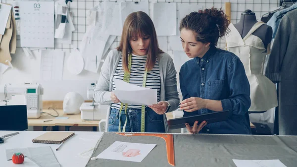 Yaratıcı giyim tasarımcıları çizimlere bakarak ve bunları tablet görüntüleri ile karşılaştırarak. Moda endüstrisi kavram başarılı başlangıç. Tekstil, dikiş makinesi ve kukla görülebilir.